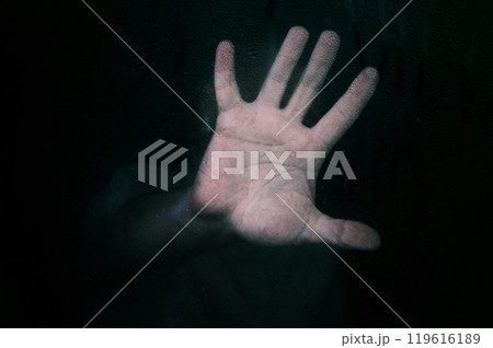 Horror scene of a man with hand against wet glass on dark background. Horror scene of a man with hand against wet glass on dark background. 119616189