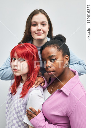 Portrait of three young women, each displaying unique styles, standing together and smiling, with one placing hand on another's shoulder, forming an intimate and friendly group bonding Portrait of three young women, each displaying unique styles, standing together and smiling, with one placing hand on another's shoulder, forming an intimate and friendly group bonding 119616271