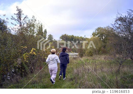 A middle-aged woman and her old mother take a morning jog together to maintain health by the river in autumn A middle-aged woman and her old mother take a morning jog together to maintain health by the river in autumn 119616853