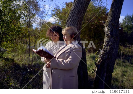 middle-aged woman and elderly mother with holy bible in hands praying for peace in autumn forest 119617131