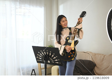 Young female musician playing electric guitar while recording a video for her social media channel 119618009
