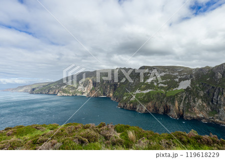 Vibrant cliffs of Slieve League rise over Atlantic under cloudy sky, creating colorful coastal scene 119618229