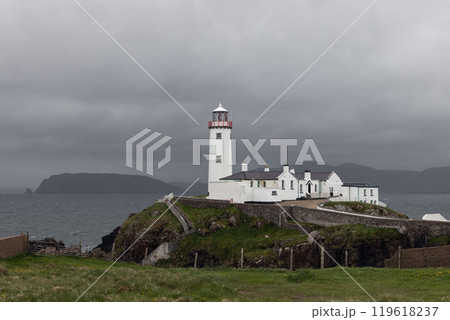 Fanad Head Lighthouse stands against grey sky and ocean as storm approaches highlighting stark white Fanad Head Lighthouse stands against grey sky and ocean as storm approaches highlighting stark white 119618237