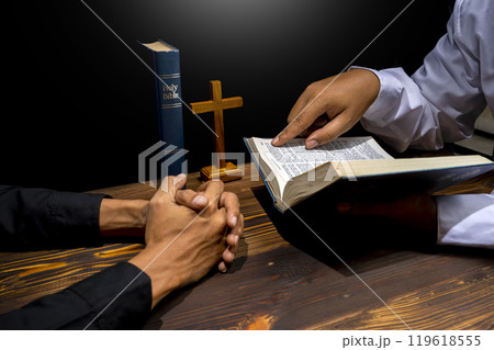Man praying together with religion cross and on a opened holy bible. Symbol of faith and worship in God. People christianity prayer in church 119618555