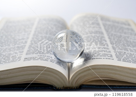 Opened book of Holy Bible with glass ball. It is laying on white background. Symbol of faith and worship in God 119618558