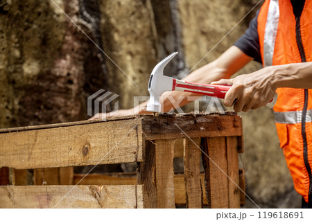 Workers in safety vest using hammer to to work assembling pallet parts 119618691