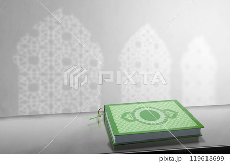 The holy book of Al Quran sitting on table with a shadow of mosque windows on the wall. Muslim holy book 119618699
