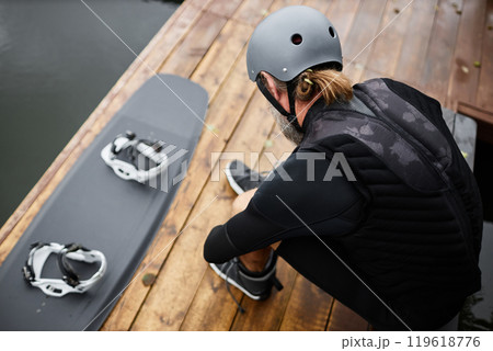 Top view of unrecognizable man putting on wakeboarding gear on wooden pier preparing for water sports outdoors copy space 119618776