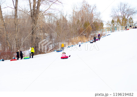 Families and friends happily slide down a snow-covered slope on inner tubes, enjoying a fun-filled winter day at an outdoor recreation area. Children and adults enjoy tubing down a snowy hill at a 119619482