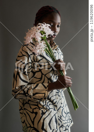 Delicate portrait of young Black woman posing with exotic flowers accentuating femininity in studio set 119620096