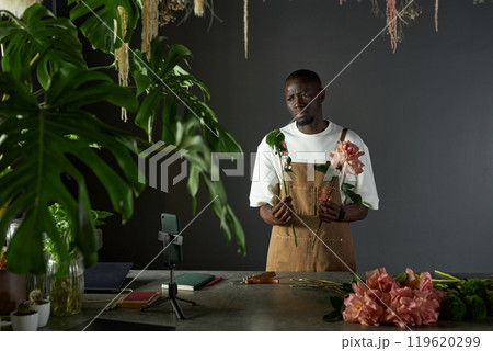 Minimal waist up portrait of young African American man as male florist designing flower bouquet and recording video for social media copy space Minimal waist up portrait of young African American man as male florist designing flower bouquet and recording video for social media copy space 119620299