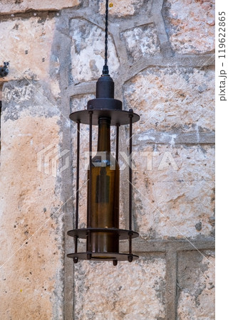 Rustic bottle-shaped lantern hanging on stone wall 119622865