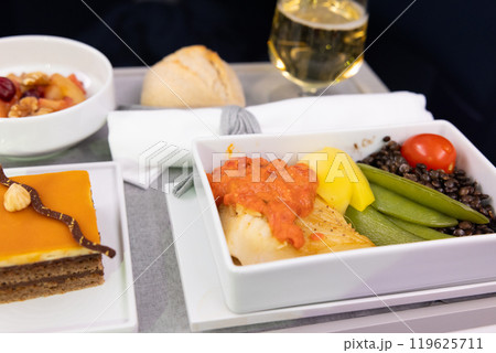おいしいビジネスクラスの機内食オヒョウの魚料理と野菜とシャンパン、チョコレートケーキ 119625711