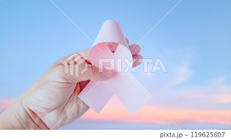 Hand holding pink ribbon, symbolizing breast cancer to enhance awareness, hope and unity, raising awareness and support for those affected by cancer, fostering understanding and prevention. Hand holding pink ribbon, symbolizing breast cancer to enhance awareness, hope and unity, raising awareness and support for those affected by cancer, fostering understanding and prevention. 119625807