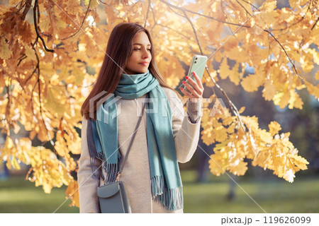 A girl with a smartphone takes photos in an autumn forest A girl with a smartphone takes photos in an autumn forest 119626099
