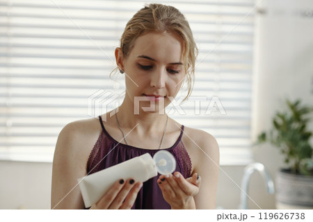 Woman Examining Cream Bottle in Kitchen Woman Examining Cream Bottle in Kitchen 119626738