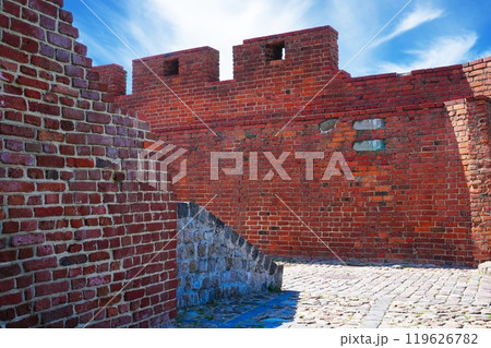 Old red brick fortress wall with two turrets under blue sky on a sunny day 119626782