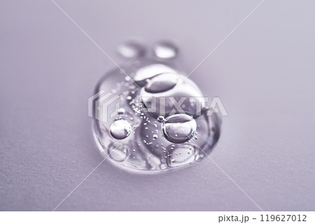 A drop of serum on a purple background. Texture of a cosmetic product. A drop of serum on a purple background. Texture of a cosmetic product. 119627012