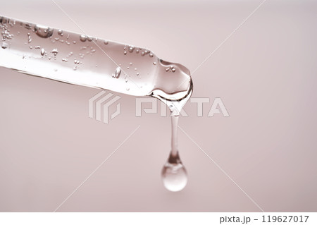 Pipette with facial serum pouring out of it on pink background. 119627017