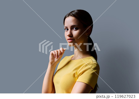 Portrait of beautiful young girl with long red hair looking at camera on grey background Portrait of beautiful young girl with long red hair looking at camera on grey background 119627023