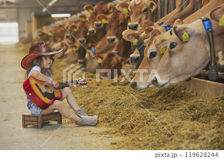 Charming child in a cowboy costume sings for cows on a farm in Denmark Charming child in a cowboy costume sings for cows on a farm in Denmark 119628244