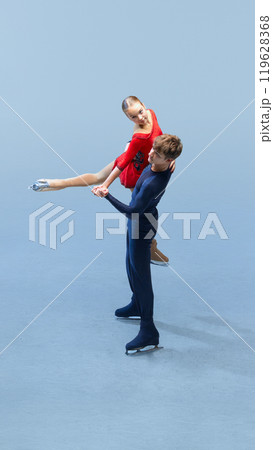 Charming, artistic man and woman on skating rink, performing figure skating tricks against cold blue background. Charming, artistic man and woman on skating rink, performing figure skating tricks against cold blue background. 119628368