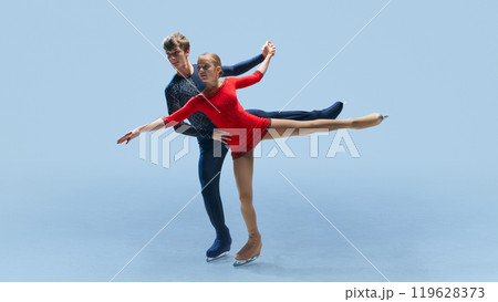 Male and female figure skating partners perform synchronized routine, showcasing their balance and athleticism against cold blue background. Male and female figure skating partners perform synchronized routine, showcasing their balance and athleticism against cold blue background. 119628373