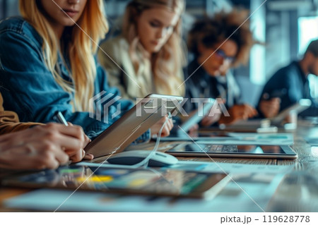 Several individuals engage in brainstorming sessions while using tablets and laptops in a contemporary work environment 119628778