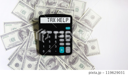 The display of the calculator says Tax Help . Dollars are lying on a white background . The display of the calculator says Tax Help . Dollars are lying on a white background . 119629031