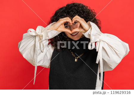 Smiling young woman makes heart gesture demonstrates love sign expresses good feelings and sympathy Smiling young woman makes heart gesture demonstrates love sign expresses good feelings and sympathy 119629316