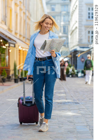 Woman tourist with suitcase exploring checking paper map search a way direction while traveling 119629329