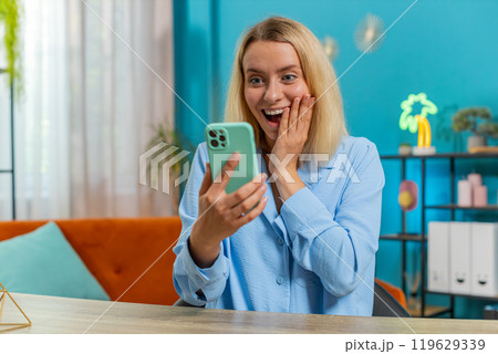 Woman freelancer using mobile smartphone receive good news celebrate victory win at home office 119629339