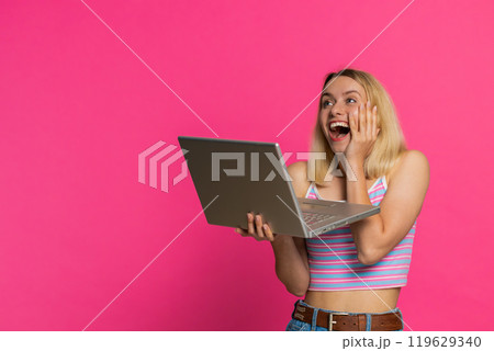 Excited happy young woman working on laptop winning online lottery game celebrating success victory 119629340