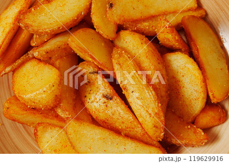 Crispy seasoned potato wedges served in a rustic bowl, a delightful snack perfect for sharing during a cozy gathering Crispy seasoned potato wedges served in a rustic bowl, a delightful snack perfect for sharing during a cozy gathering 119629916