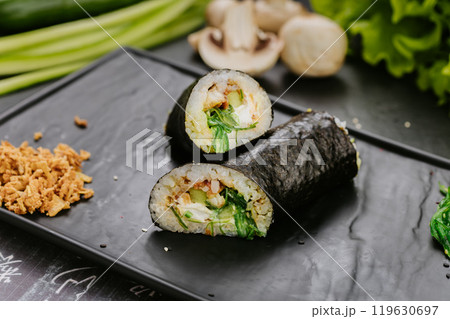 Fresh gimbap roll with chicken, vegetables, and seaweed served on a black plate with garnish 119630697