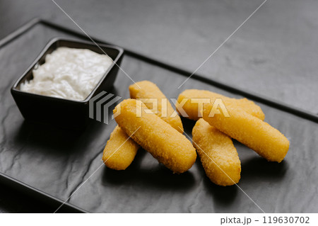 Golden crispy cheese sticks with a creamy dip, served on a sleek black plate. Perfect appetizer Golden crispy cheese sticks with a creamy dip, served on a sleek black plate. Perfect appetizer 119630702