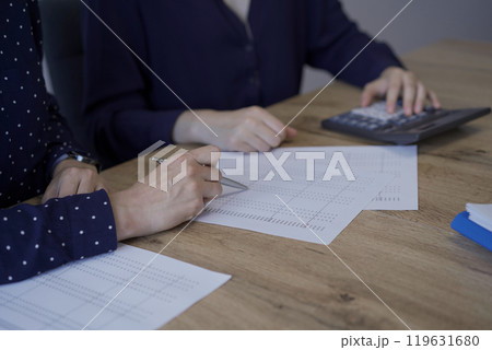 Accountants or auditors reviewing financial documents while sitting at the wooden desk in office. Professionals analyzing paper reports and using calculators, close up view. Audit and taxes Accountants or auditors reviewing financial documents while sitting at the wooden desk in office. Professionals analyzing paper reports and using calculators, close up view. Audit and taxes 119631680