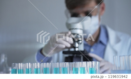 Laboratory tubes are in focus, closeup view. Man scientist researcher with a white protective gloves is using a microscope at the background. Medicine and science Laboratory tubes are in focus, closeup view. Man scientist researcher with a white protective gloves is using a microscope at the background. Medicine and science 119631942