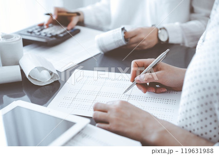 Two accountants use a calculator and tablet computer for counting taxes or revenue balance. Business, audit, and taxes concepts 119631988