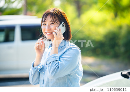 車の横でスマホで電話をかける女性 119639011