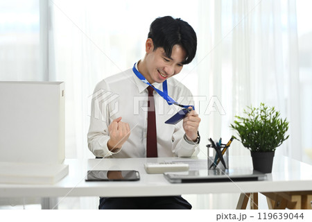 Cheerful office worker celebrating new job with ID badge in hand Cheerful office worker celebrating new job with ID badge in hand 119639044