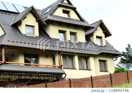 Three-story wooden beige house with complex roof structure. 119640748
