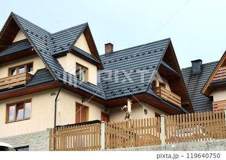 Three-story wooden beige house with complex roof structure. 119640750