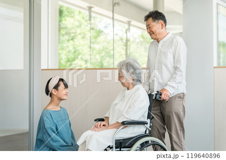 介護施設を訪れた孫娘と車椅子の祖母と祖父（お見舞い・老人ホーム・介護・入院・病院） 119640896
