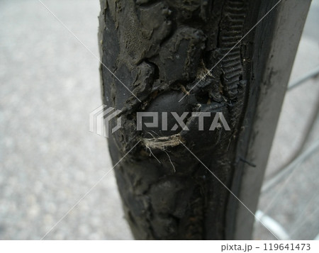 劣化と摩耗でタイヤに穴が開き、中のチューブが風船のように膨らんで露出している危険な状態の自転車の後輪 119641473