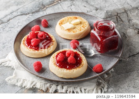 Hot fresh breakfast crumpets with butter melting, jam and fresh raspberries closeup on the plate. Horizontal 119643594