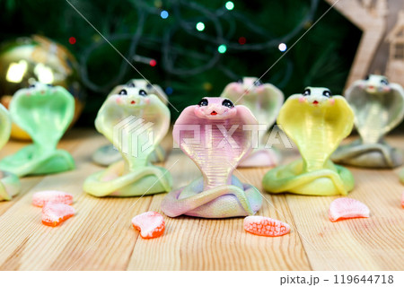 Snake - handmade soap, symbol of the future 2025. Christmas-style composition against the background of garlands and fir-tree branches Snake - handmade soap, symbol of the future 2025. Christmas-style composition against the background of garlands and fir-tree branches 119644718