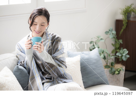 部屋で温かいコーヒーや飲み物を飲むかわいい女性　秋冬のリラックスするイメージ　広角 119645097