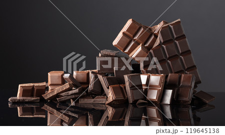 Broken bitter and milk chocolate bars on a black background. 119645138
