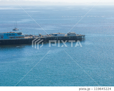 The image captures Santa Cruz Wharf in California, extending into the Pacific Ocean. Several buildings and boats are visible against the blue water and clear sky. 119645224
